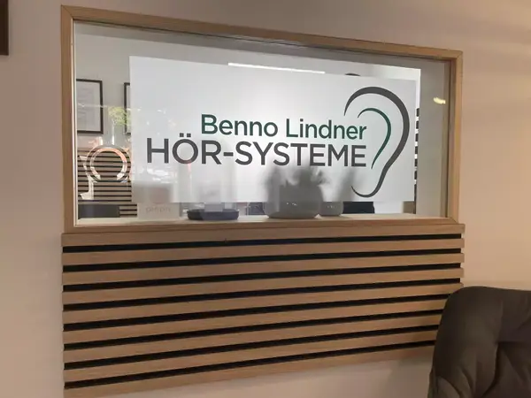 Praxisfenster mit Schild von Benno Lindner Hörsysteme und stilisiertem Ohr-Logo.