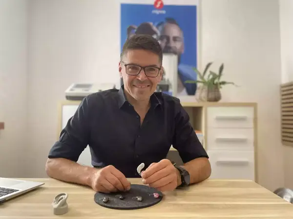 Hörakustiker präsentiert moderne Hörgeräte Beratung im Fachgeschäft am Holztisch.