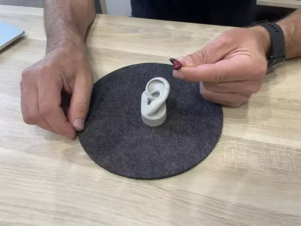 Ein Mann hält ein Hörgerät vor ein Modell-Ohr auf einem Tisch zur Hörgeräteanpassung.